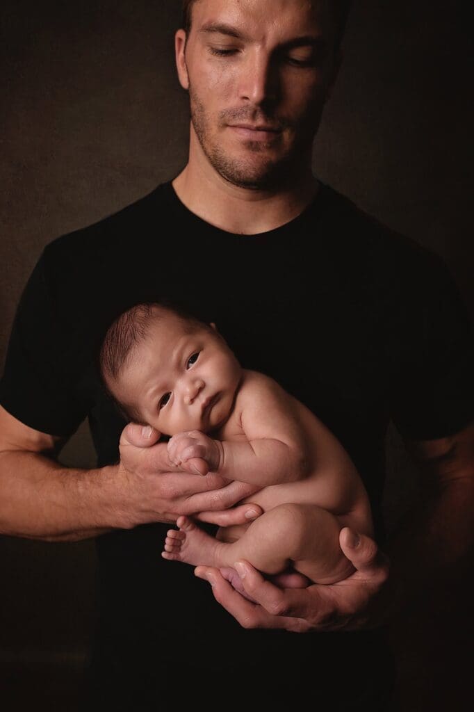 Father gently cradling his awake newborn during a fine art Nashville newborn photography session, creating a timeless father and baby portrait.