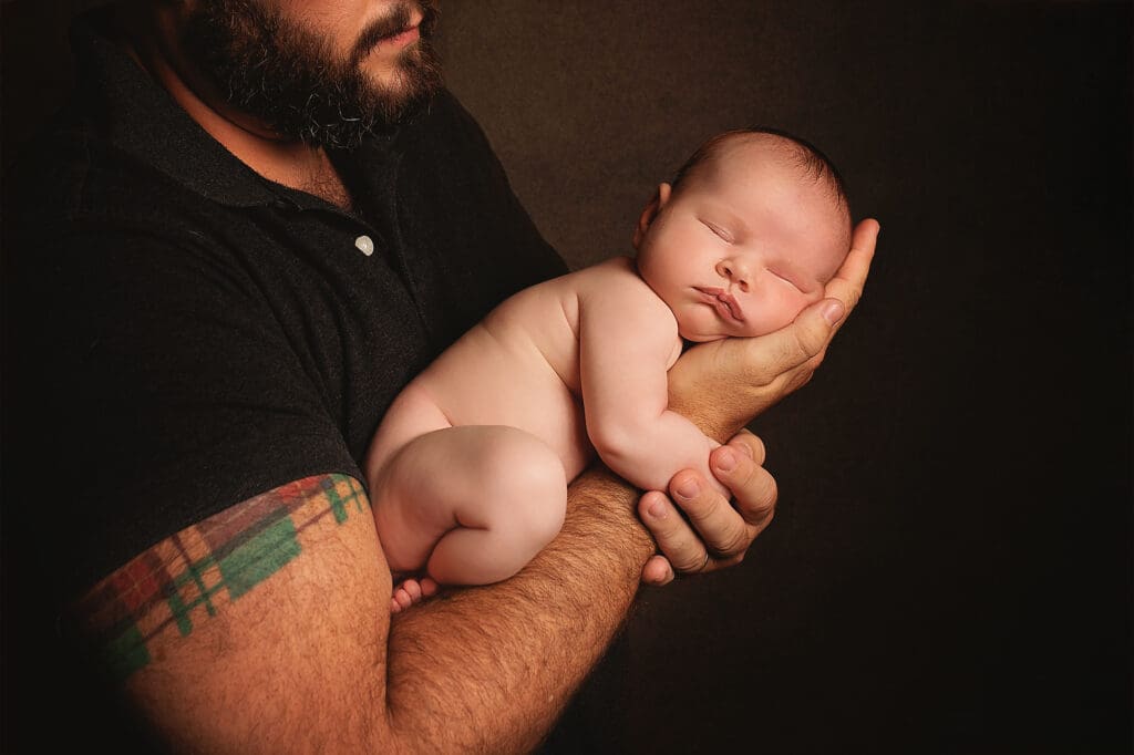 Father gently cradling his sleeping newborn during a fine art Nashville newborn photography session, highlighting the bond between dad and baby.