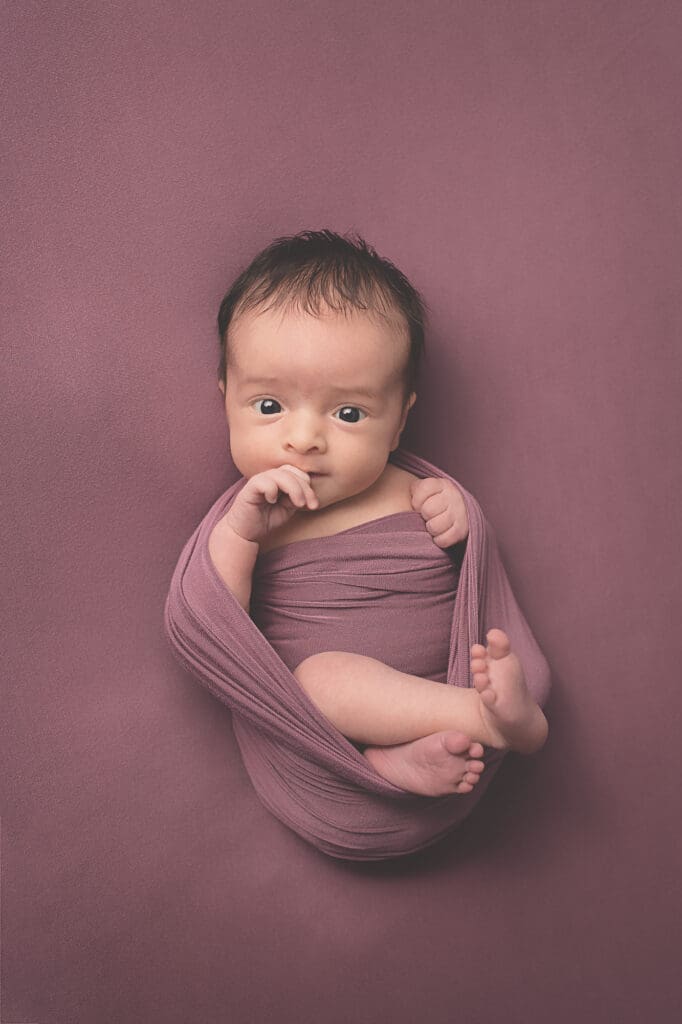 Awake newborn wrapped in a soft mauve swaddle, gazing toward the camera during a fine art Nashville newborn photography session.