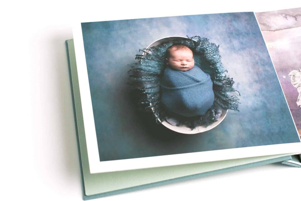 Heirloom newborn photo album featuring a fine art portrait of a sleeping baby wrapped in a blue knit swaddle on the cover.
