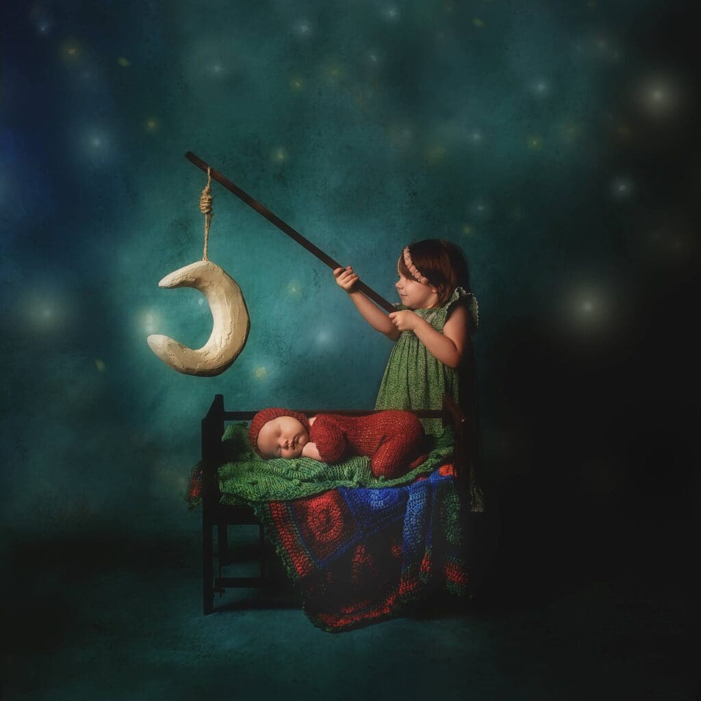 Older sibling pretending to fish for the moon above a sleeping newborn in a tiny bed, creating a whimsical fine art portrait against a starry blue backdrop.