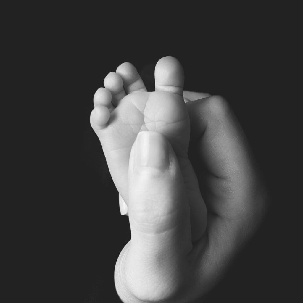 Close-up black and white photograph of a newborn baby's tiny foot cradled in a parent's hand during a Nashville newborn photography session.