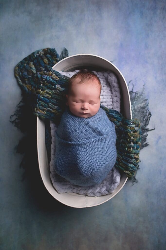 Sleeping newborn wrapped in a soft blue swaddle and nestled in a cozy basket during a fine art Nashville newborn photography session.
