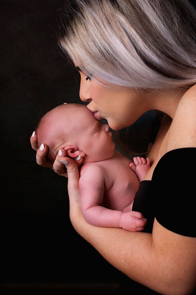Mother gently kissing her sleeping newborn during a fine art Nashville newborn photography session, capturing a tender mother and baby moment.