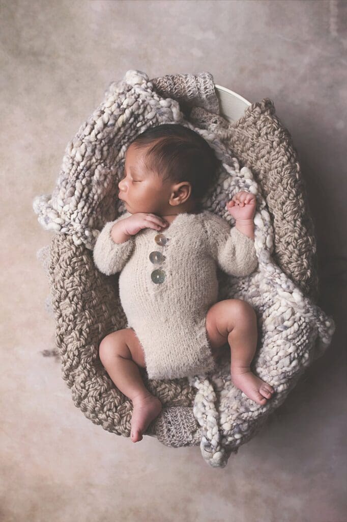 Sleeping newborn in a soft knit romper resting in a cozy basket with chunky knit blankets during a fine art Nashville newborn photography session.