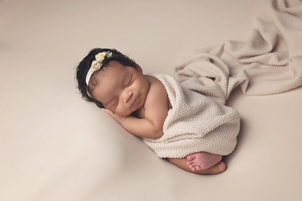 Peacefully sleeping newborn baby girl wrapped in a soft cream blanket during a timeless Nashville newborn photography session with neutral styling.