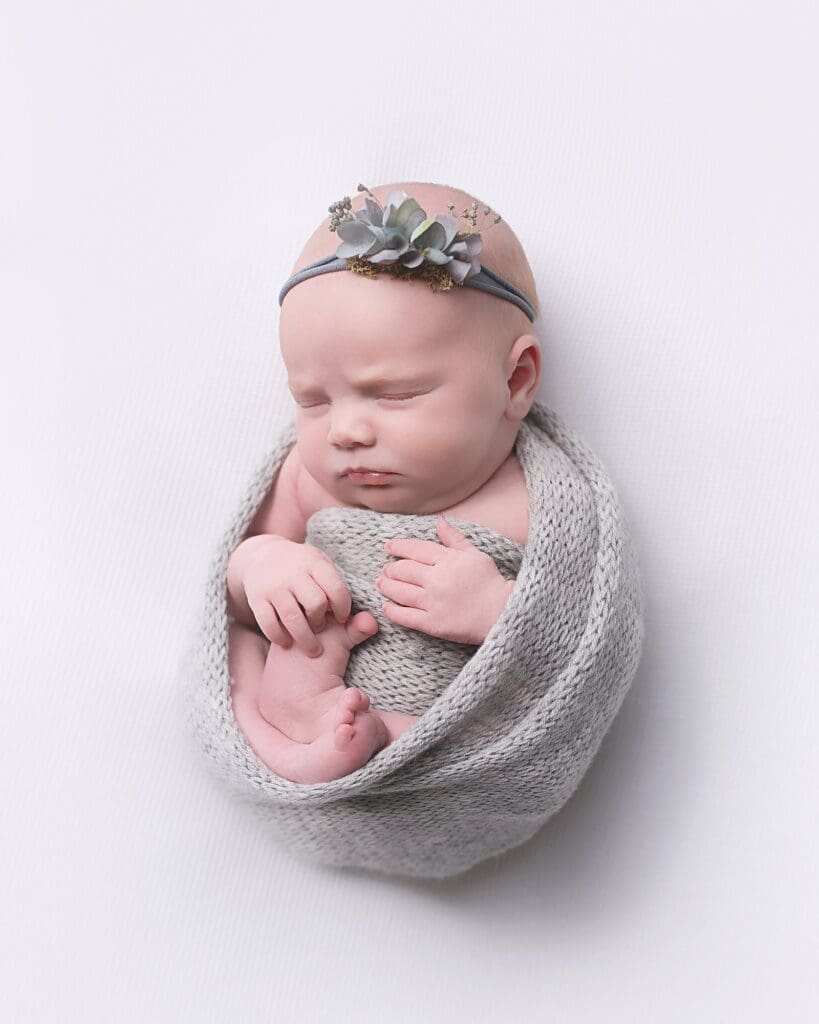 Newborn baby girl wrapped in a soft gray knit wrap with a delicate floral headband during a classic Nashville newborn photography session.