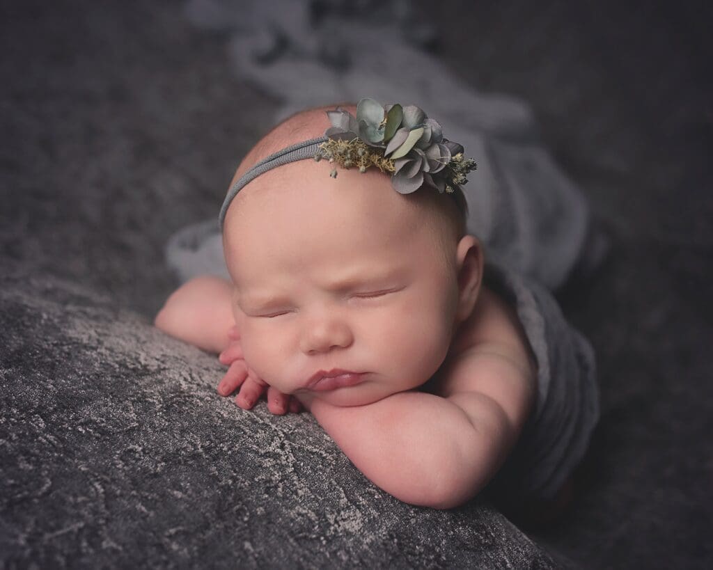 Sleeping newborn baby wearing a delicate floral headband, resting peacefully on soft gray fabric during a Nashville newborn photography session.