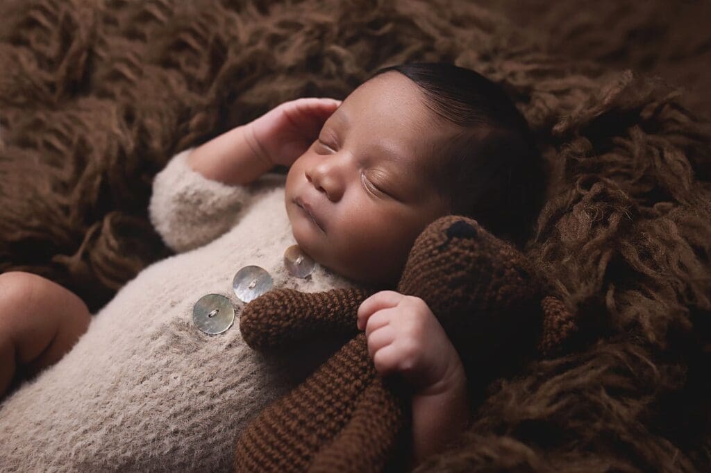 Peacefully sleeping newborn cuddling a handmade teddy bear on a cozy brown blanket, photographed during a Nashville newborn photography session.