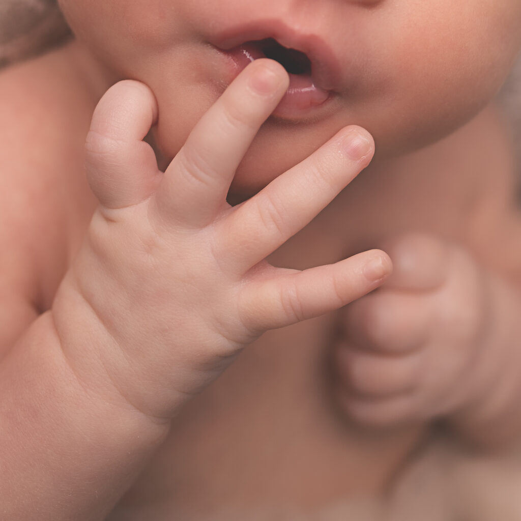 Close-up detail of a baby's tiny hand reaching toward their lips, highlighting soft fingers, delicate skin, and natural curiosity during a Nashville milestone photography session.