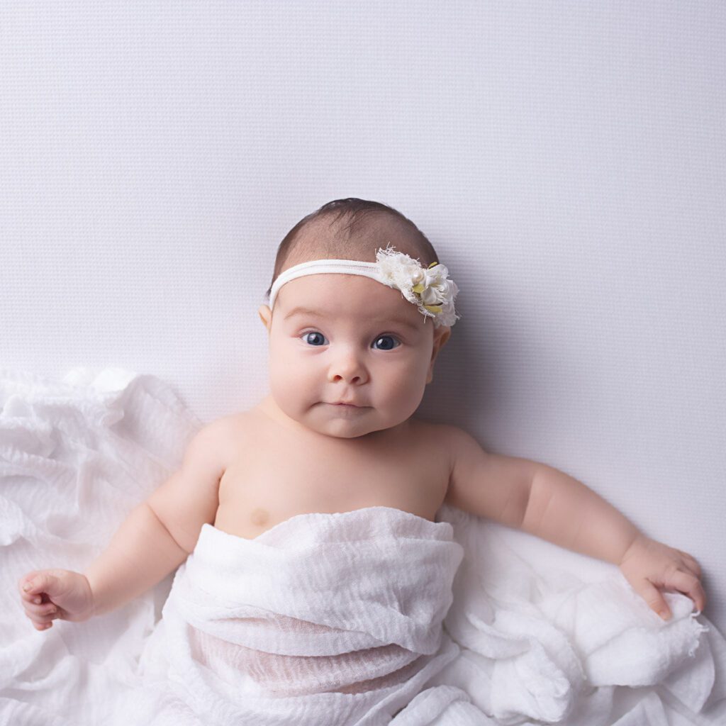 Awake baby wrapped in soft white fabric with a delicate floral headband during a Nashville baby photography session.
