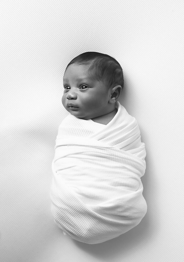 Awake newborn baby swaddled in white in a simple black-and-white portrait by a Nashville newborn photographer.