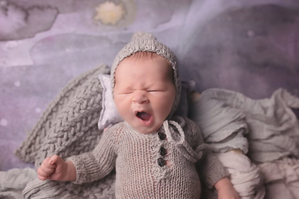 Yawning newborn baby wearing a soft gray knitted outfit and bonnet during a Nashville newborn photography session.