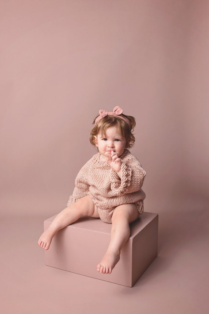 Toddler in a soft pink knit outfit sitting on a pink block during a Nashville milestone photography session.
