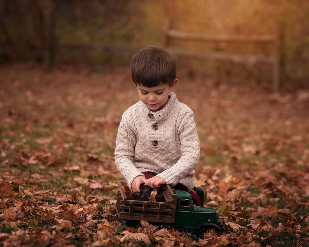 Young boy playing with a vintage green toy truck in fallen autumn leaves during a Nashville child photography session.