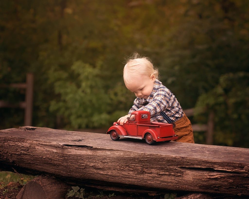 Blond toddler playing with a vintage red toy truck on a rustic wooden log outdoors in Middle Tennessee.