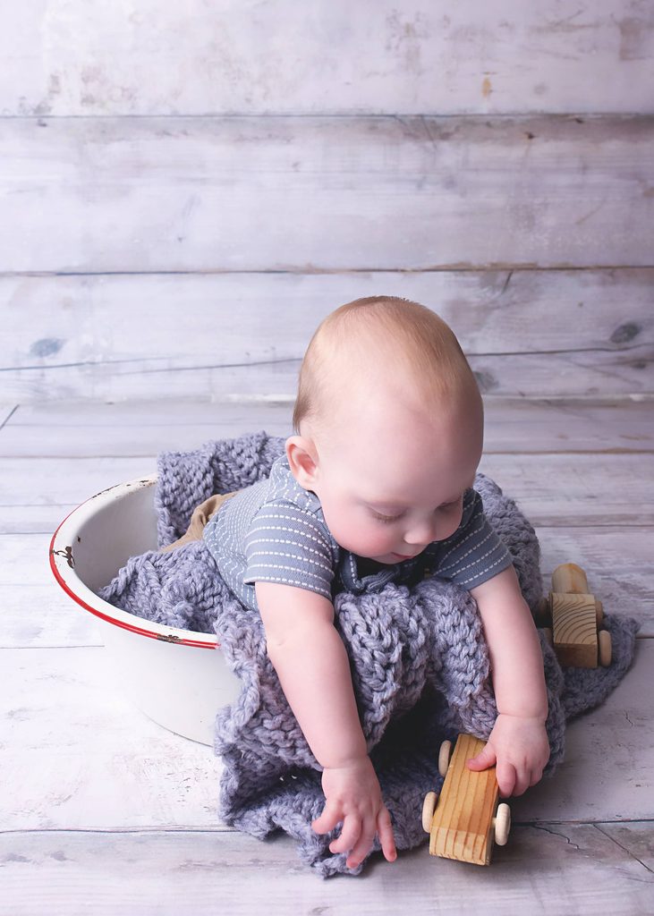 Baby boy playing with wooden toys beside a vintage enamel basin and chunky knit blanket during a Nashville baby photography session.