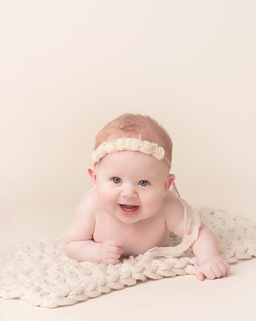 Smiling baby girl wearing a delicate floral headband during a soft neutral milestone portrait session.