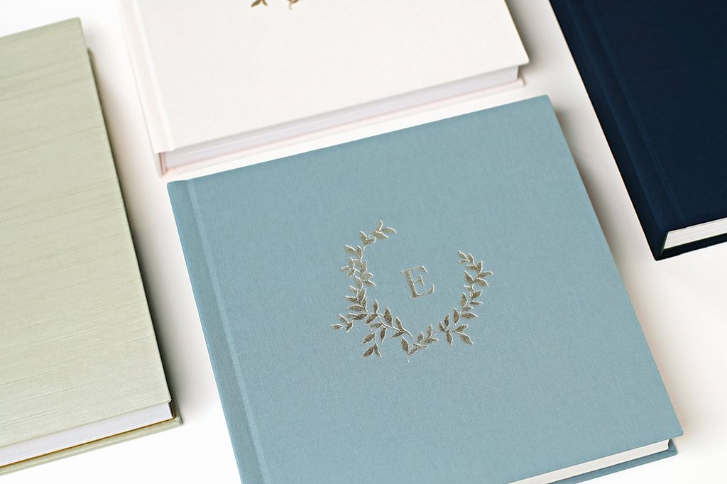 Luxury linen-covered heirloom photo albums in soft blue, ivory, sage green, and navy, featuring elegant personalized cover designs and embossing.