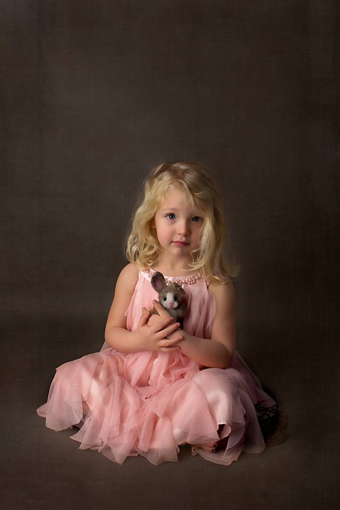 Young blond girl in a pink dress holding a small stuffed bunny for a timeless fine art child portrait in Nashville.