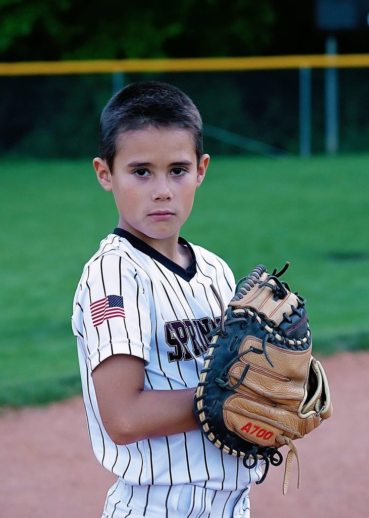 Young boy in a pinstriped baseball uniform holding his glove and looking seriously at the camera during a Nashville children's portrait session.
