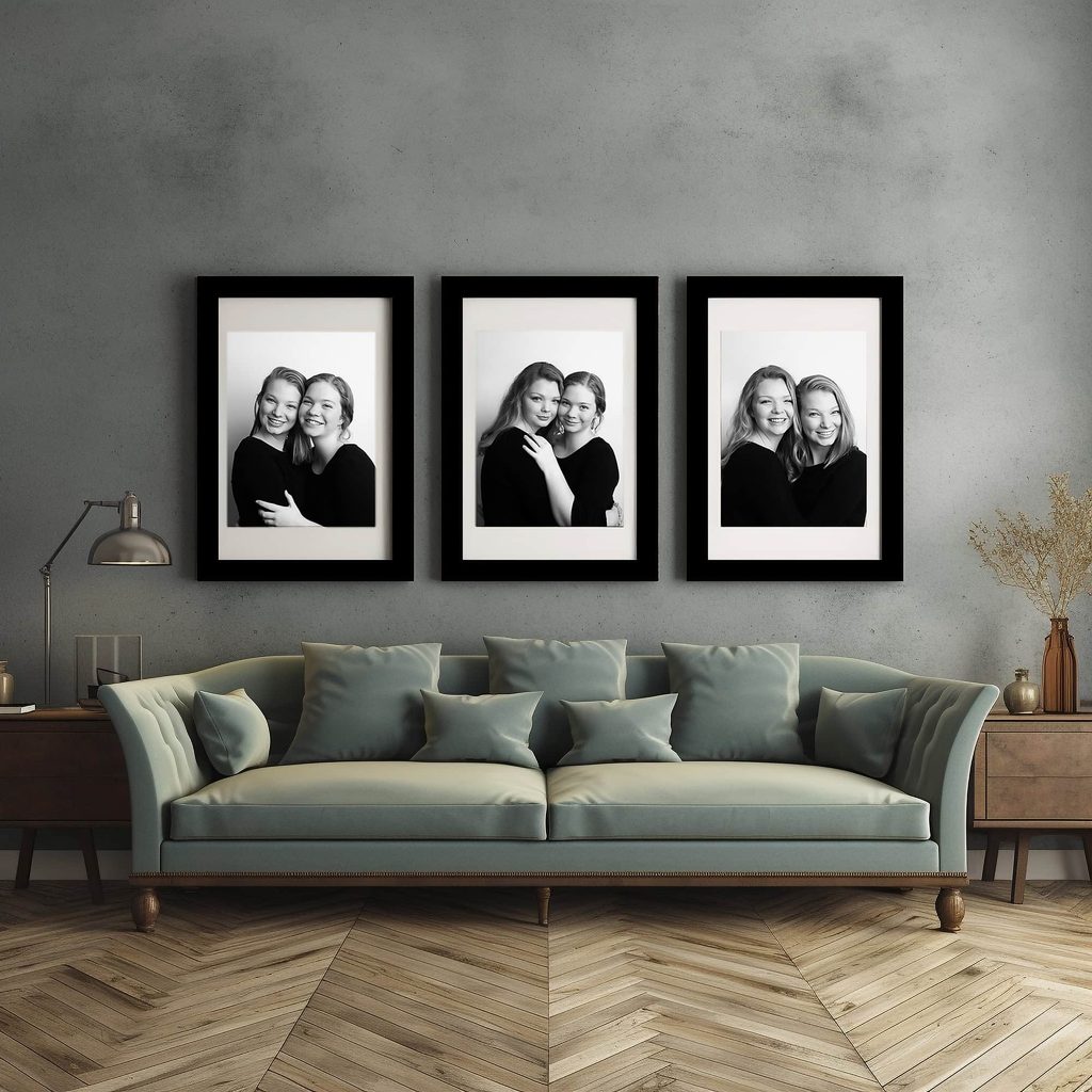 Three black-and-white fine art portraits of three sisters displayed in matching black frames above a sage green sofa, creating an elegant heirloom wall gallery.