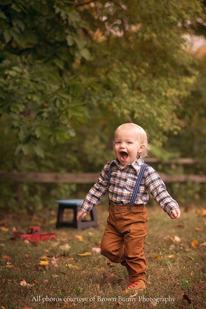Laughing blond toddler boy running through an autumn setting during a playful Nashville child photography session.